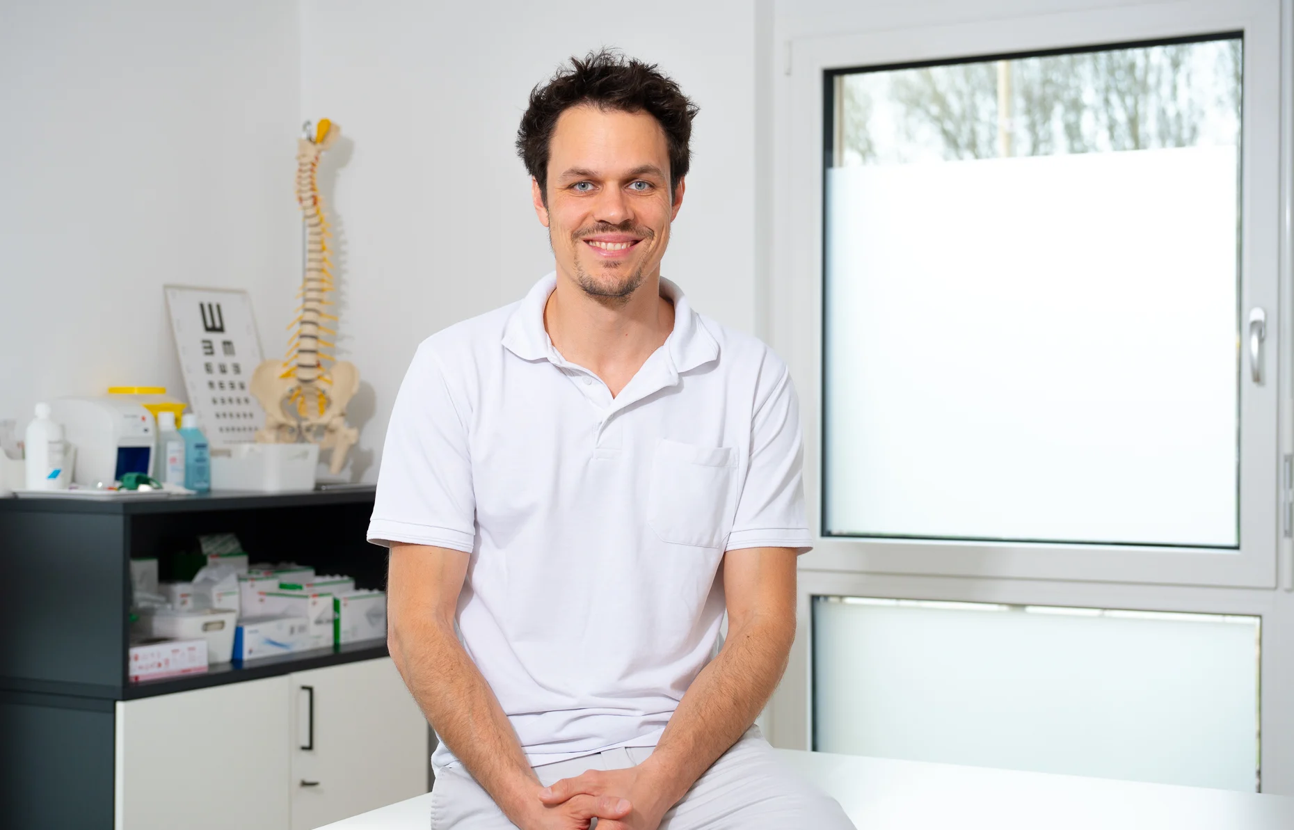 Dr. Patrick Hain sitzt im Behandlungsraum auf der Liege